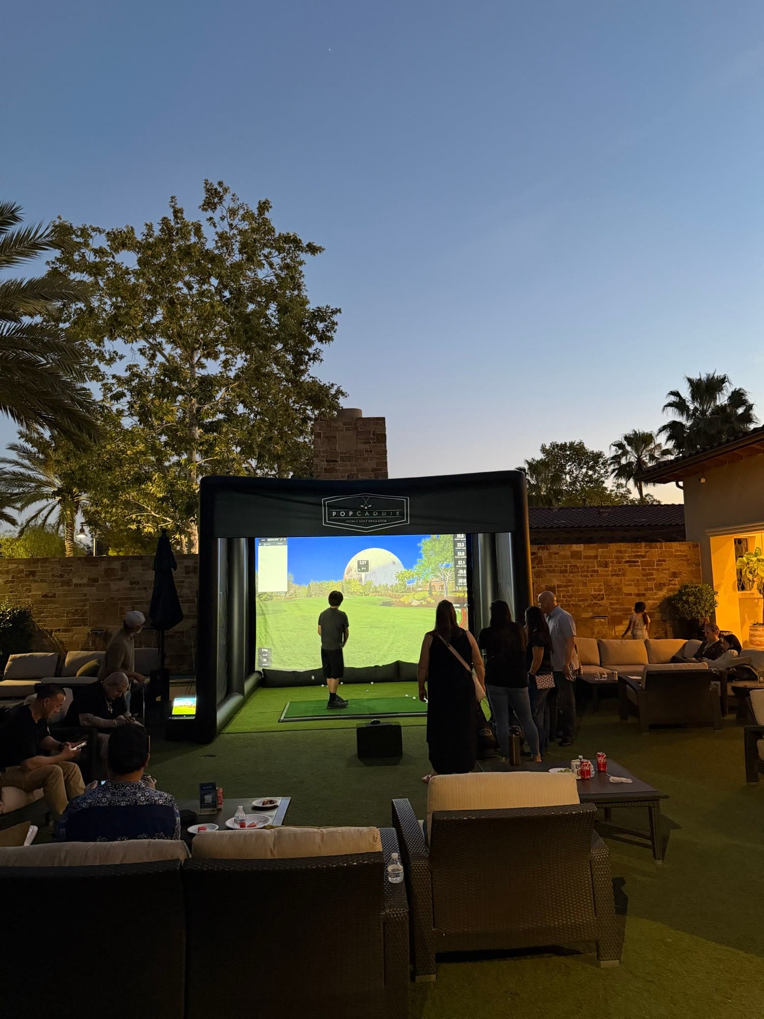 Invitados jugando al simulador de golf en una terraza al anochecer (evento de PopCaddie)